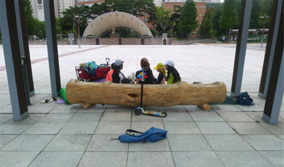 양산시가 폐목재를 활용해 제작한 통나무 의자에 시민들이 앉아 휴식을 취하고 있다.